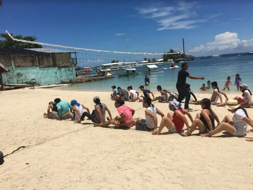 A facilitator guiding teams seated in rows during a beach team building game