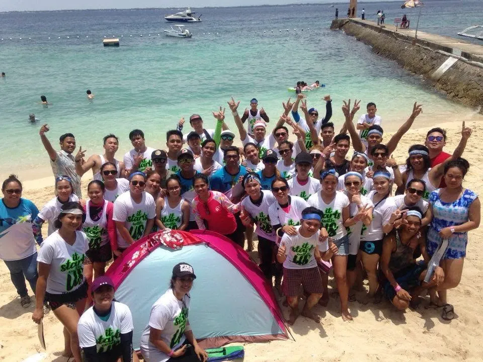 A large group in matching shirts cheering on the beach during a Steps team building day
